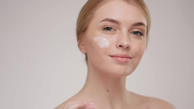 Slow motion portrait young woman uses creams of her face. Concept for fresh moisturized skin beautiful closeup cosmetic face happy healthy model. Young blonde hair woman take care of her skin.