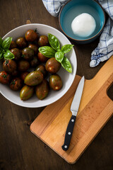 Gestreifte bunte Tiger Tomaten in Schale mit Mozzarella und Basilikum mit Geschirrtuch und Messer auf Holz Brett 