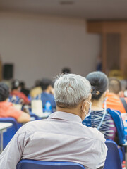 Back view of Asian man wear protective face mask to prevent Coronavirus(COVID-19) sitting on a chair for social distancing in  auditorium. Conference concept in coronavirus pandemic.Selective focus.