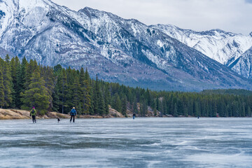 Tourists doing ice-skating in Johnson Lake frozen water surface in winter time. Snow-covered...