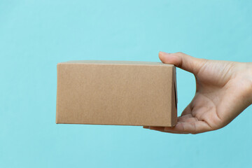 Woman hand hold the brown corrugated box on blue wall background with copy space