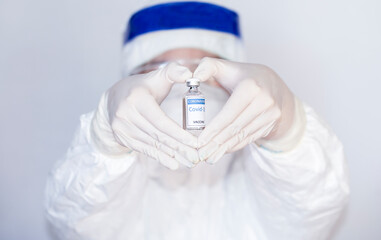 Doctor or nurse wearing ppe suit, mask, face shield holding COVID-19 coronavirus vaccine with a vial in the hand wearing gloves form a heart shape, Breakthrough for immunization coronavirus 2019.