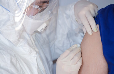 Fototapeta premium Doctor or nurse wearing ppe suit, mask, face shield and injection covid 19 vaccine to patient at upper arm. Doctor injection vaccine for stimulating the body to build immunity against COVID-19.