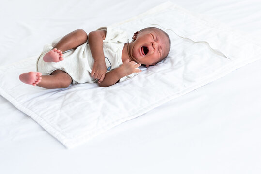Portrait images of half African half Thai, 12-day-old baby newborn son, lying on a white bed and is crying, to infant and family concept.