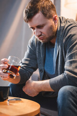 frustrated man holding glass of whiskey while sitting at home alone