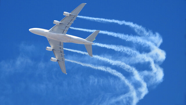 Ultra wide zoom photo of passenger airplane leaving white smoke trails in deep blue sky while flying at high altitude