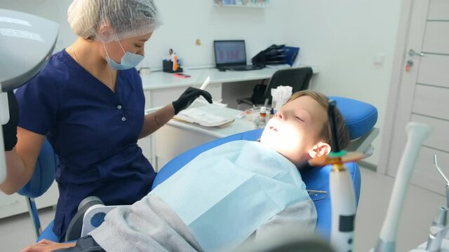 Child boy is in dentist's chair, doctor is preparing to preventive examination in stomatology clinic. Checkup of teen's teeth. Dentistry concept. Oral hygiene and teeth care and stomatology cure.