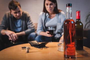 bottles of alcohol and empty wallet on table near drunk couple on blurred background
