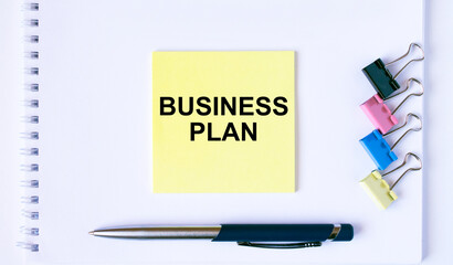 Yellow sticker with text Business Plan lying on a white Notepad with a pen and paper clips
