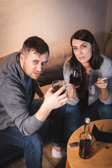 alcohol-addicted couple looking at camera while holding glasses of whiskey and wine