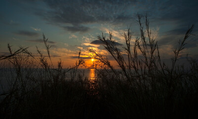 A relaxing photo of sunset whose lights are reflected in the sea and spread through the cloudy sky.