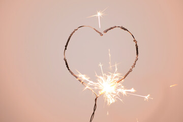 Heart shape sparkler
burning on a delicate pink background with love background concept.