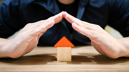 Property ownership concept. Home loan insurance. male hand protecting and covering over house toy model on wooden table.