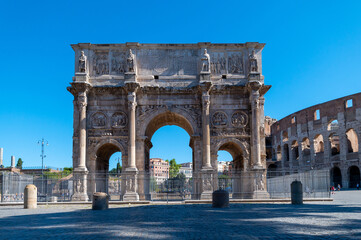 Fototapeta na wymiar Arch of Constantine near the Colosseum and the Arch of Titus. Photographed in summer with few tourists, blue sky and clouds. Celebrates the victory of Constantine over Maxentius. Rome, Italy.