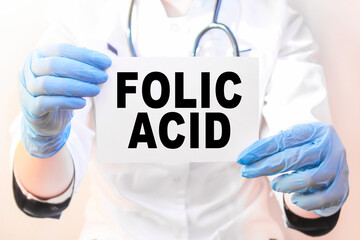 The doctor's blue - gloved hands show the word FOLIC ACID - . a gloved hand on a white background. Medical concept. the medicine