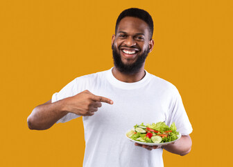 African Man Pointing Finger At Salad Standing On Yellow Background