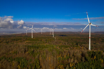 Fototapeta na wymiar wind farm in a colorful autumn forest with blue sky