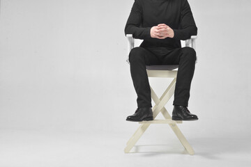 A man without a face in black clothes sits in the director's chair on a white background in the studio