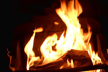 Closeup of dancing flames with dark background of burning wooden logs in fireplace, warming light in Christmas holidays