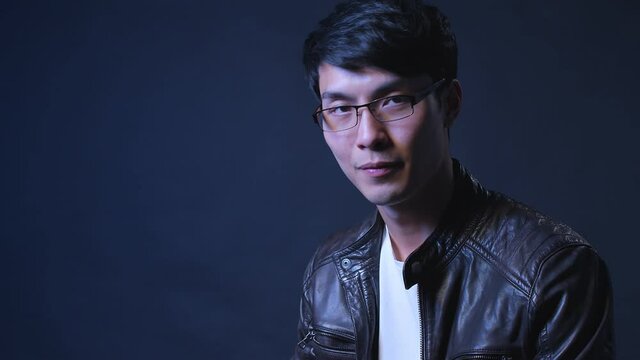 asian handsome attractive male wearing glasses and leather jacket thinking concentrate emotion studio shot dark background