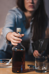 partial view of alcoholic woman taking bottle of whiskey from table, blurred background
