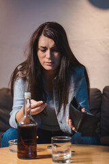 drunk woman holding empty wallet near glass and bottle of whiskey on blurred foreground