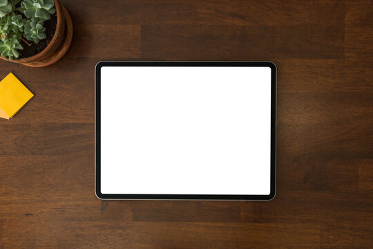 Overhead view of a modern black tablet pc with blank white screen on a home wooden office table and work desk