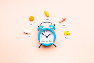 medicine drugs daily and weekly schedule concept. assorted drugs near alarm clock. above view. drug medication reminder conceptual. pink background