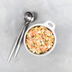 Russian vegetable salad olivier with salmon in a bowl on a light gray background top view