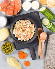 Russian vegetable salad olivier with red fish in a wooden bowl on a light gray background top view in rustic style 