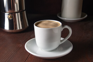 a white mug with espresso coffee, a geyser coffee maker and a burning candle nearby