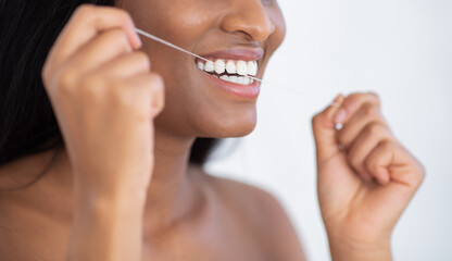 Beautiful smiling african american female holding dental floss, cleaning teeth, remove food between tooth