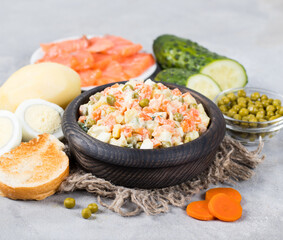 Traditional russian vegetable salad olivier with red fish in a wooden bowl on a light gray background in rustic style 