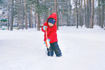 Fototapeta na wymiar Little boy kid shoveling snow on home drive way. Beautiful snowy garden or front yard. Child with shovel playing outdoors in winter season. Kids play outside.