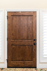 The interior view of a classic brown stained solid wood front door with windows and plantation...