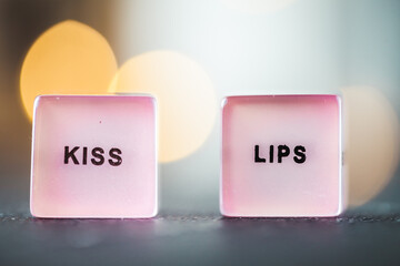 Macro shot of the pink dice with kiss lips text on them. Blurred background with bokeh lights. Happy valentine's day. Love game. Gambling