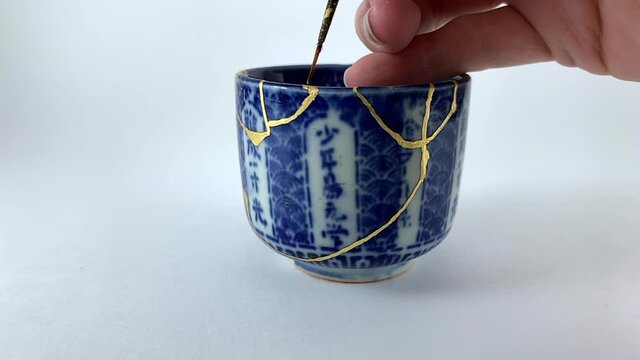 Artisan working on kintsugi process. Slow motion cinematic Kintsukuroi video. Applying gold phase.