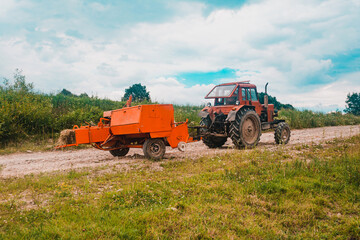 Obraz premium The process of harvesting hay for cattle, a tractor making bales in the field, old machinery.