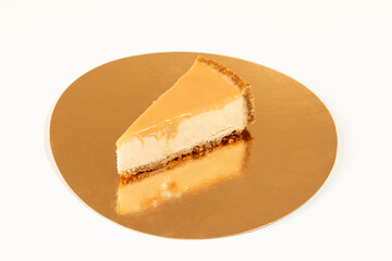 piece of caramel cheesecake on a golden plate on white background