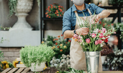 Florist at work. Millennial pretty young man owner in apron and protective mask make fashion modern...