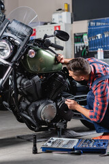 Fototapeta na wymiar mechanic making diagnostics of motorcycle in workshop near toolbox