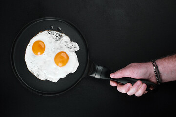 Fried Eggs In A Frying Pan in male hand on black background, copy space