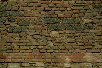 Old weathered irregular brick wall texture with exposed rows of bricks in assorted sizes and shapes in a full frame view