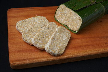 tempeh wrapped in banana leaves and tempeh slices on a wooden cutting board