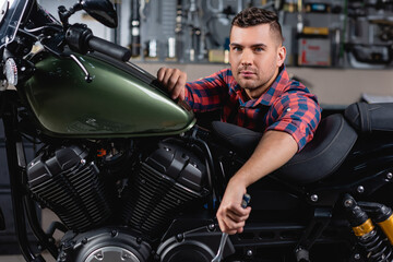 Fototapeta na wymiar young mechanic looking at camera near motorcycle in workshop