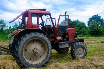 Old red tractor in the field during the haymaking season, pressing hay on bales, forage harvesting.