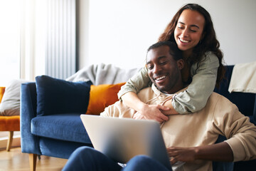 Relaxed Young Couple At Home Sitting On Sofa Browsing Internet On Laptop Computer
