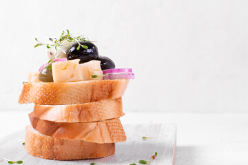 Pickled cheese, olives and red onion with microgreen on stack of baguette pieces on the white board