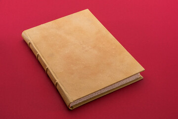Antique book with light brown leather hardcover on cardinal red background
