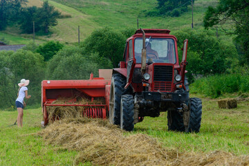 Obraz premium Old red tractor in the field, Ukrainian fields and old machinery, hay harvesting in the field. Girl rakes the grass with a rake.